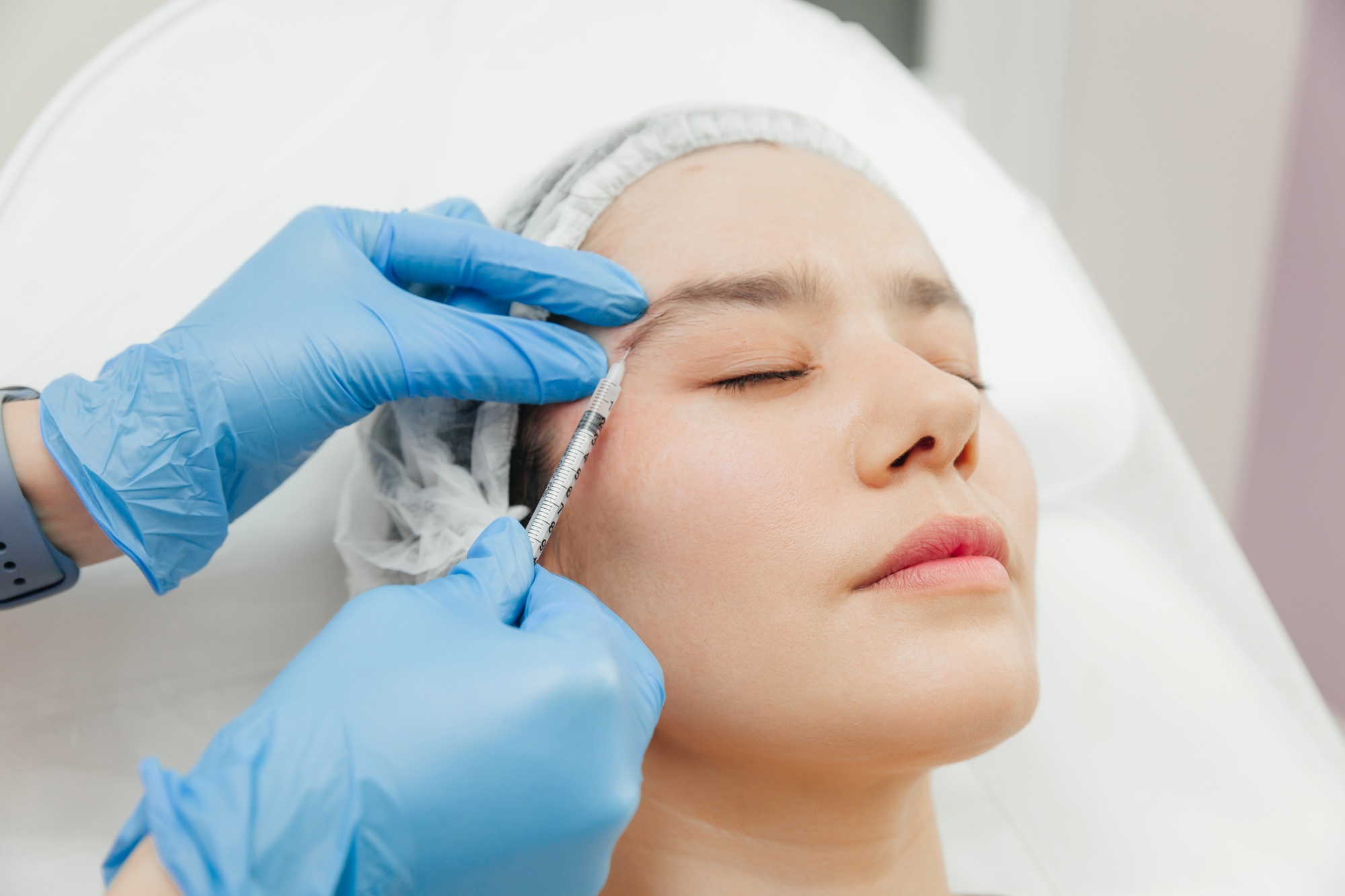 Close-up of the hands of a beautician injecting Botox into a woman's forehead.