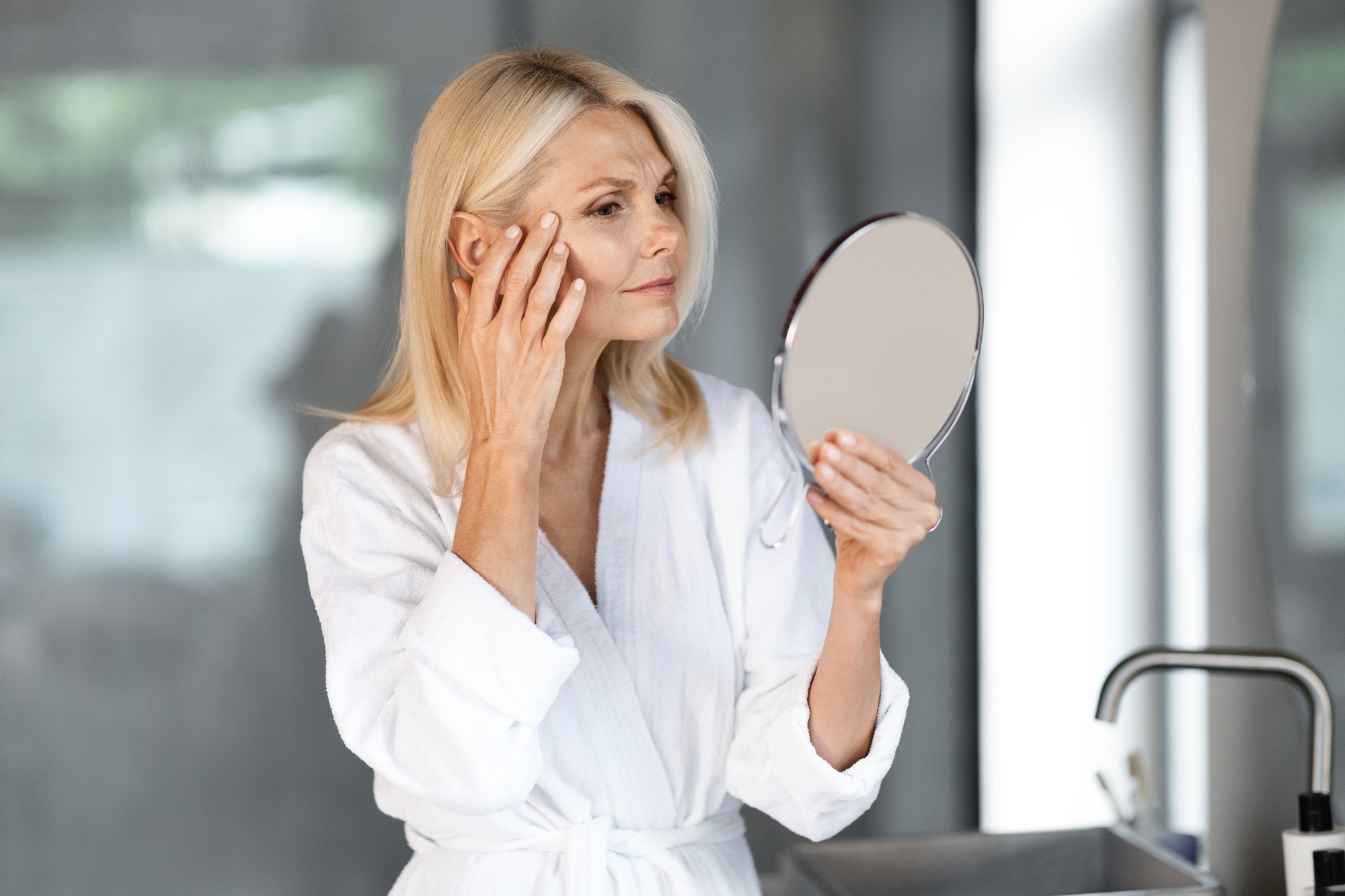 Skin Aging. Mature Woman Holding Mirror And Looking At Wrinkles Near Eyes
