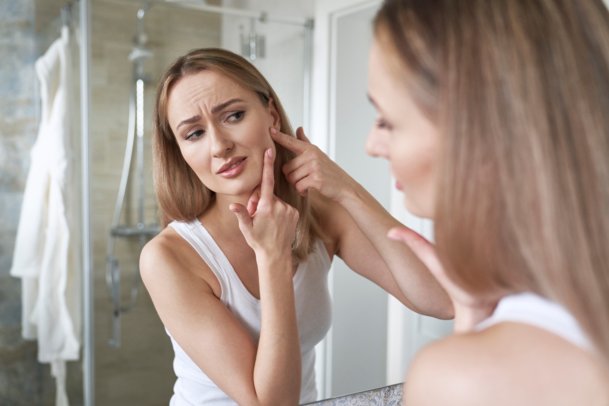 Young caucasian woman in the bathroom having acne problems with face